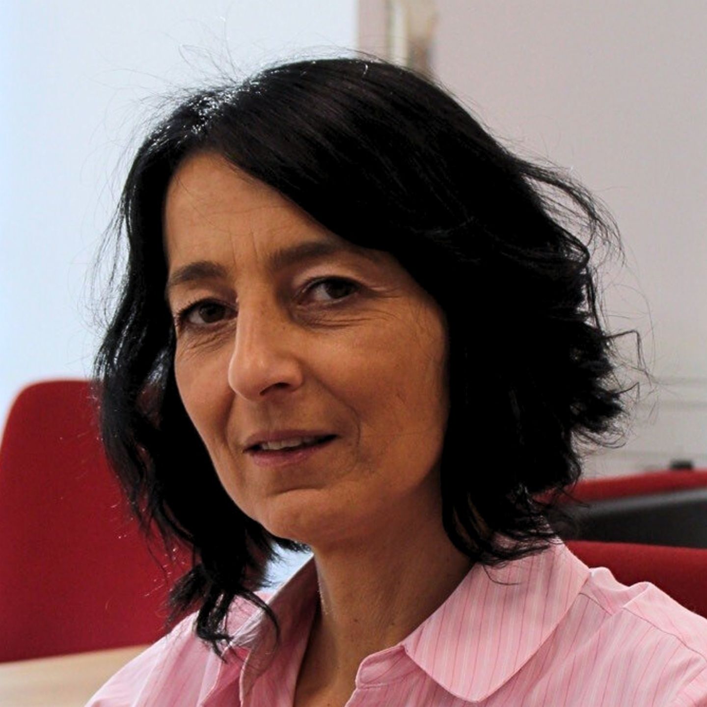 Cristina Pasere, manažerka Compliance Operations Support ve společnosti EOS Romania, sedí u svého stolu v růžové pruhované halence a dívá se do kamery.