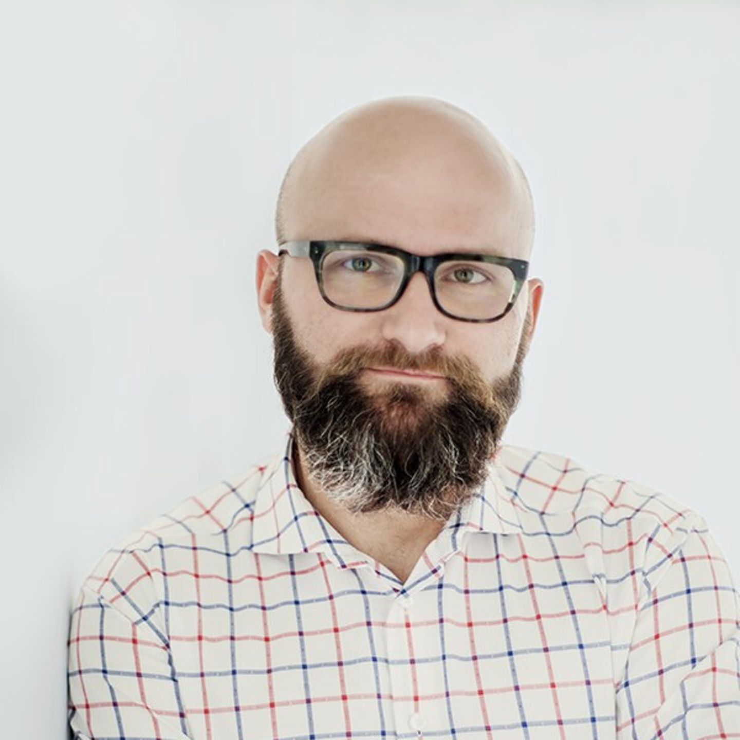 Dr. hab. Tomasz Piekot v košili s kostkovaným vzorem opřený o bílou zeď.