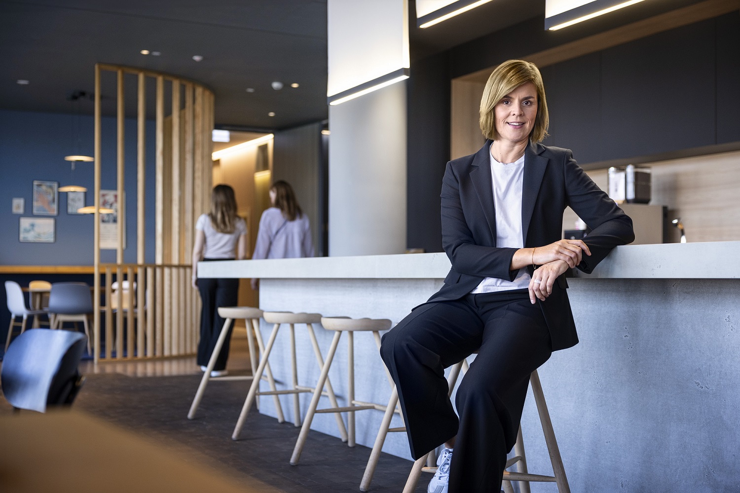 Dr. Eva Griewel, finanční ředitelka (CFO) skupiny EOS, sedí v společenském prostoru na vysokém stoličce, oblečená v černém bleyzeru.
