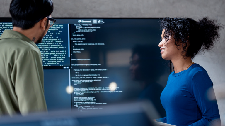 AI v inkasu: Na tomto obrázku dva profesionálové společně analyzují programový kód pro automatizované procesy na velkém displeji. Scéna ilustruje praktickou aplikaci umělé inteligence (AI) a robotizované automatizace procesů (RPA) v řízení pohledávek – příklad digitální transformace v managementu pohledávek.