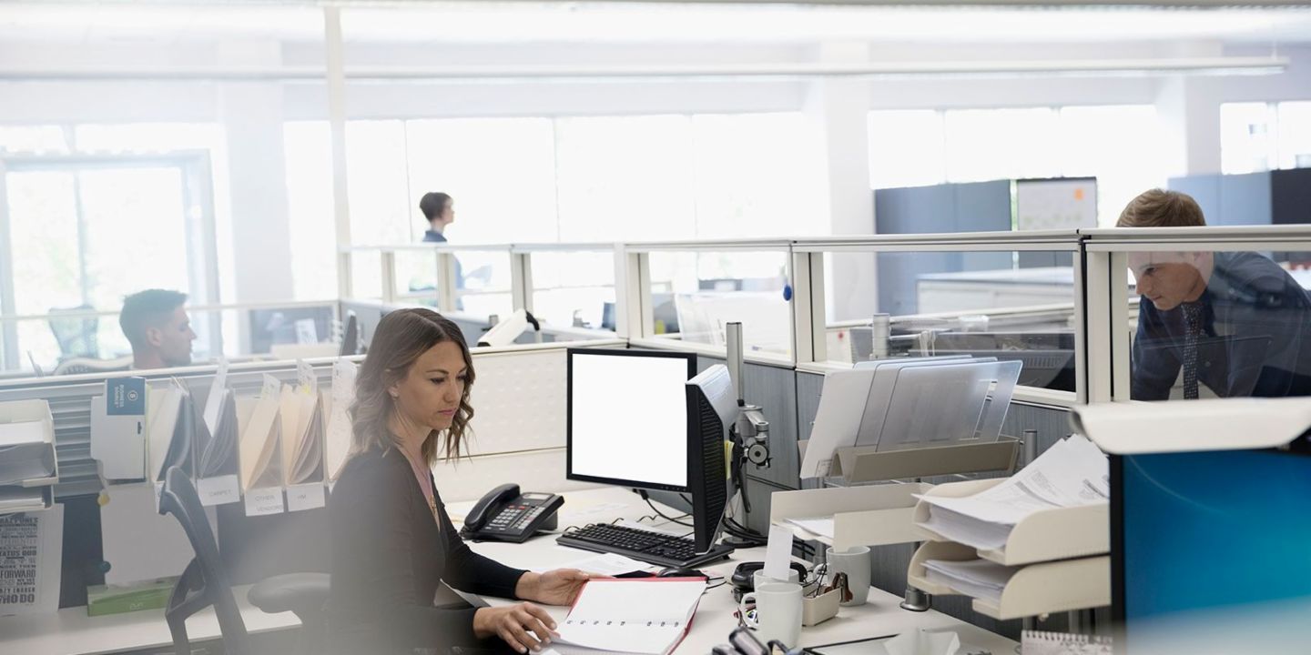 Digitalizace: Tři zaměstnanci v open space kanceláři, jedna žena sedí mezi papíry a svým počítačem